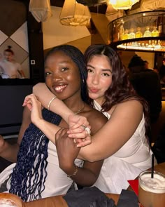 two women sitting at a table hugging each other