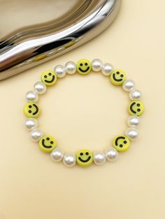 a bracelet with smiley faces and pearls on it next to a heart shaped silver object