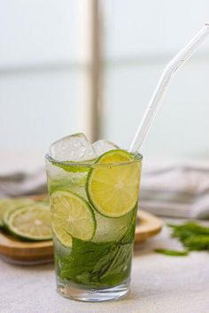 a glass filled with ice and limes on top of a table next to sliced cucumbers