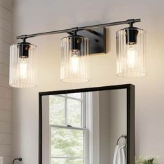 a bathroom vanity with two lights and a mirror above it, in front of a window