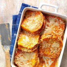 a casserole dish filled with cheese and bread slices on a blue towel next to a spatula