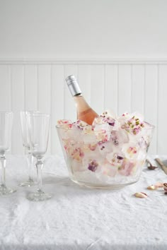 a glass bowl filled with flowers next to two wine glasses and a bottle of champagne