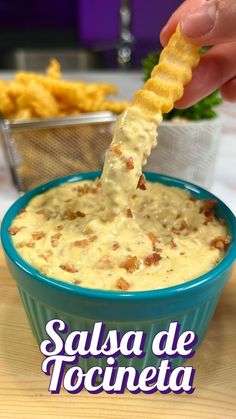 a person dipping cheese into a blue bowl filled with chips and dip sauce on the side