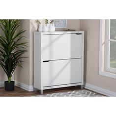 a white cabinet with two drawers next to a potted plant