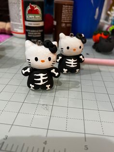 two hello kitty skeleton keychains sitting on top of a table next to each other