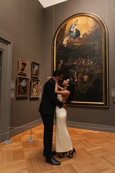 a man and woman are kissing in front of a large painting on display at an art museum