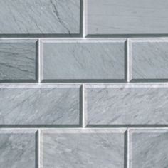 a close up view of a white brick wall with grey and white marble tiles on it