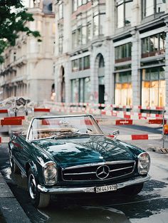 an old mercedes sits parked on the side of the road