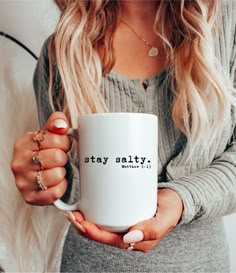 a woman holding a white coffee mug with the words stay salty in black on it