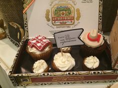 three cupcakes with white frosting and red decorations in a box on a table