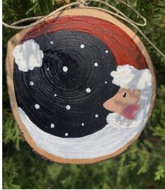 a wooden ornament hanging from a tree with snow and clouds painted on it