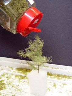 a small green plant in a white vase on top of a blue tablecloth next to a red coffee cup