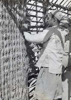 an old black and white photo of a man standing next to a fence holding something in his hand