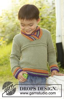 a young boy wearing a green sweater and holding a ball in his hands while standing on the grass