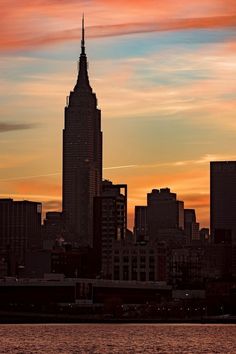 the city skyline is silhouetted against an orange and blue sky