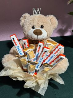 a teddy bear sitting on top of a table with candy bars in it's lap