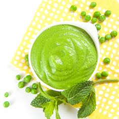 a small white bowl filled with green sauce and peas on top of a yellow napkin