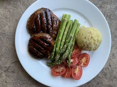 a white plate topped with steak, asparagus and tomatoes next to mashed potatoes