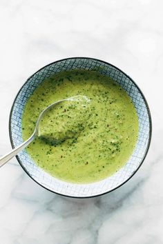 a bowl filled with broccoli soup on top of a white tablecloth next to a spoon