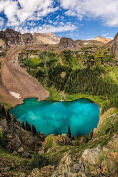 a blue lake surrounded by mountains under a cloudy sky