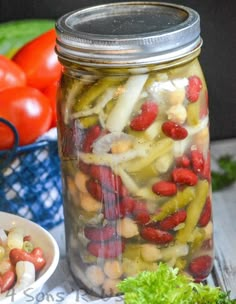 a mason jar filled with pickles and other vegetables next to a bowl of tomatoes