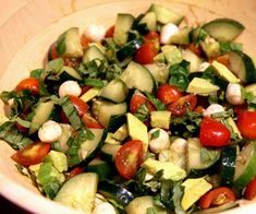 a white bowl filled with cucumber, tomatoes and other vegtables