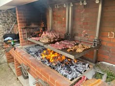 an outdoor bbq grill with meat and vegetables cooking on it's sides, in front of a brick wall