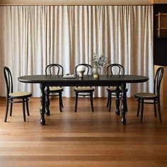 a dining room table with four chairs and a vase on top of it in front of a curtained wall