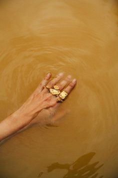 a person's hand reaching for a piece of gold in the water with their fingers