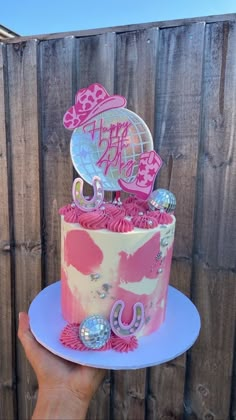 a pink and white birthday cake sitting on top of a blue plate next to a fence