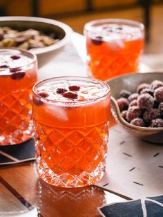 two glasses filled with liquid sitting on top of a table next to bowls of berries