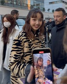 a woman holding up a cell phone in front of a man wearing a face mask