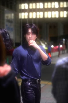 a man in blue shirt and black pants standing on street next to people with cell phone