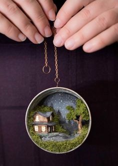 a person holding a small round ornament with a house on it's side