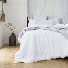 a bed with white linens and pillows in a small room next to a wooden floor