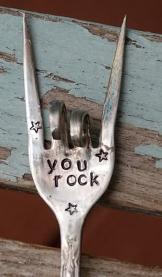 a fork with writing on it hanging from the side of a wooden wall next to a piece of wood