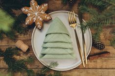 a white plate topped with green napkins next to a gold fork and christmas tree decoration