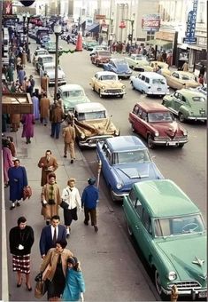 an old photo of cars and people walking down the street