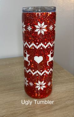 a red glitter tumbler with white snowflakes and hearts on it, sitting on a wooden table