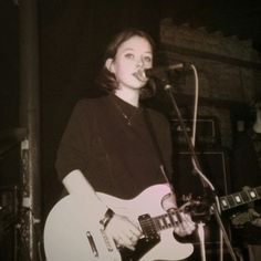 a woman singing into a microphone and playing an electric guitar in front of a microphone