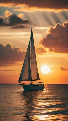 a sailboat in the ocean at sunset with sunbeams behind it and clouds