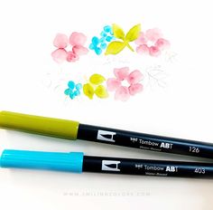 two markers are sitting next to each other on a white surface with flowers painted on it