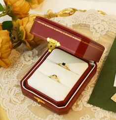 an open ring box sitting on top of a table next to some flowers and cards