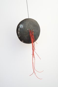 a rock hanging from a string with red wires attached to it's sides and on the wall