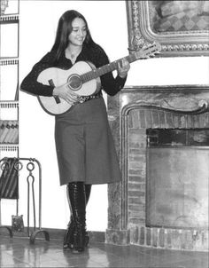 a woman standing in front of a fire place holding a guitar