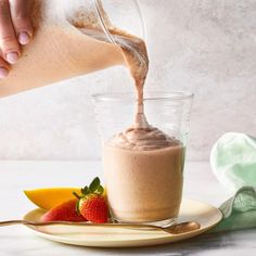 a person pouring chocolate into a glass cup with strawberries and bananas on the side