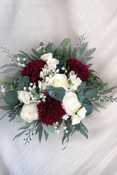 a bouquet of white and red flowers on a white sheet with greenery around it