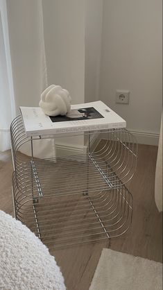 a book is sitting on top of a wire shelf next to a white bed and window