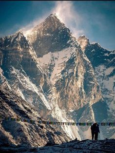 two people walking up the side of a mountain with snow covered mountains in the background