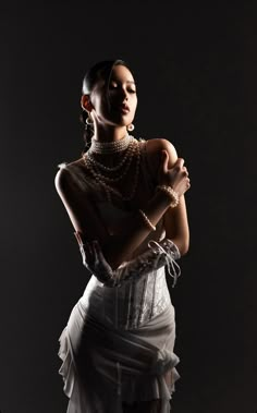 a woman in a white dress with pearls on her neck and hands folded over her chest